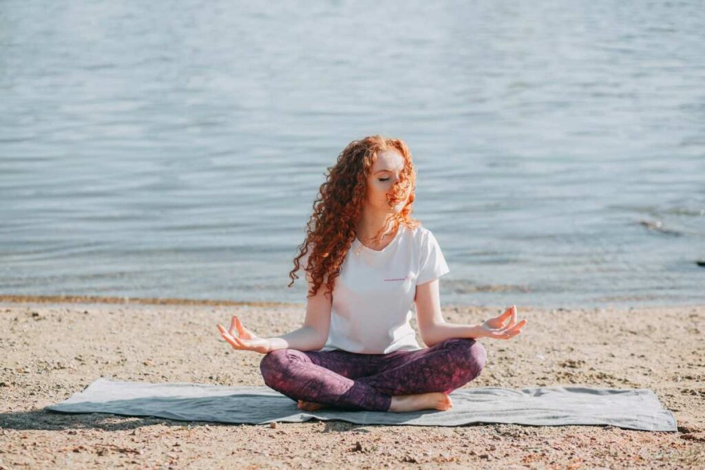 Woman practicing mindfulness meditation by the water to reduce anxiety