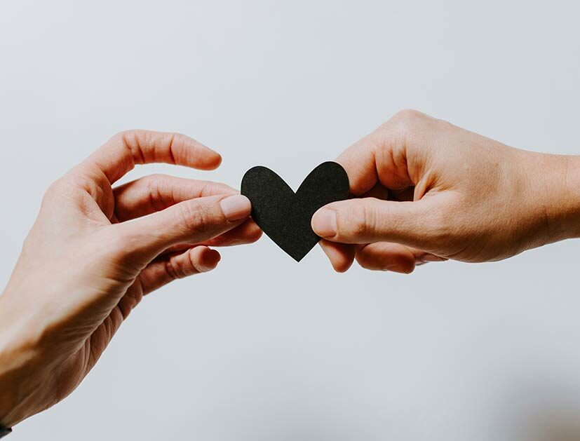 Two hands holding a small paper heart.